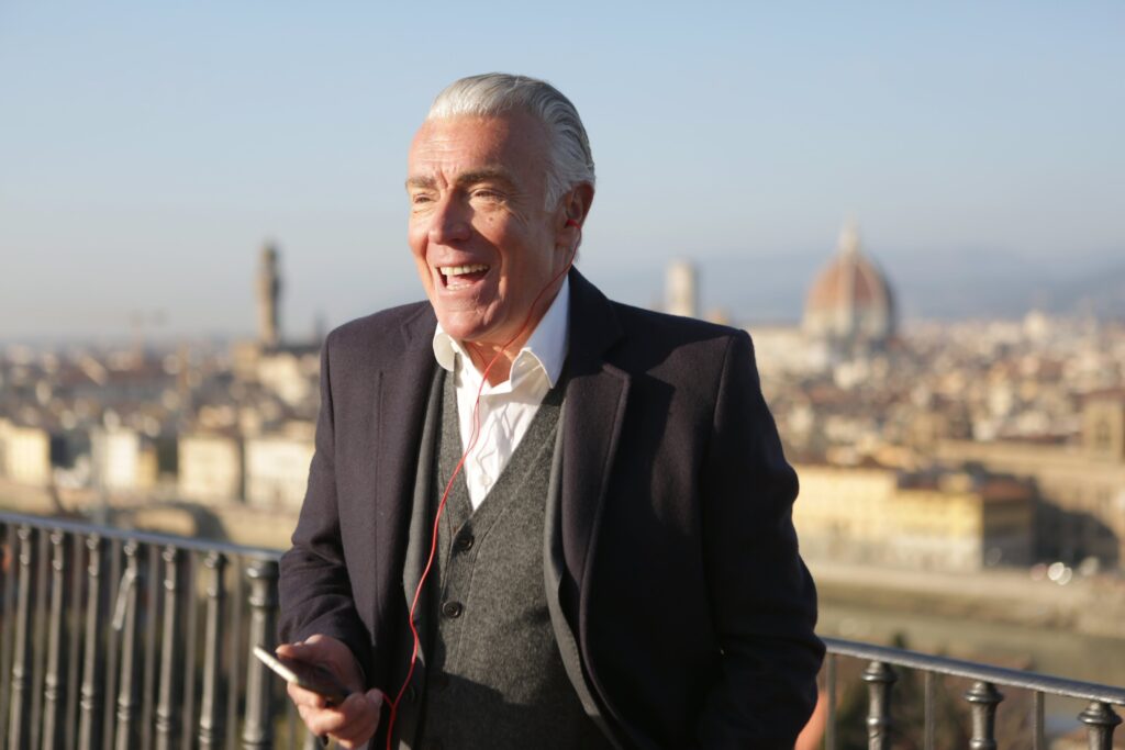 Happy elderly man with earphones smiling outdoors with a city view in the background.